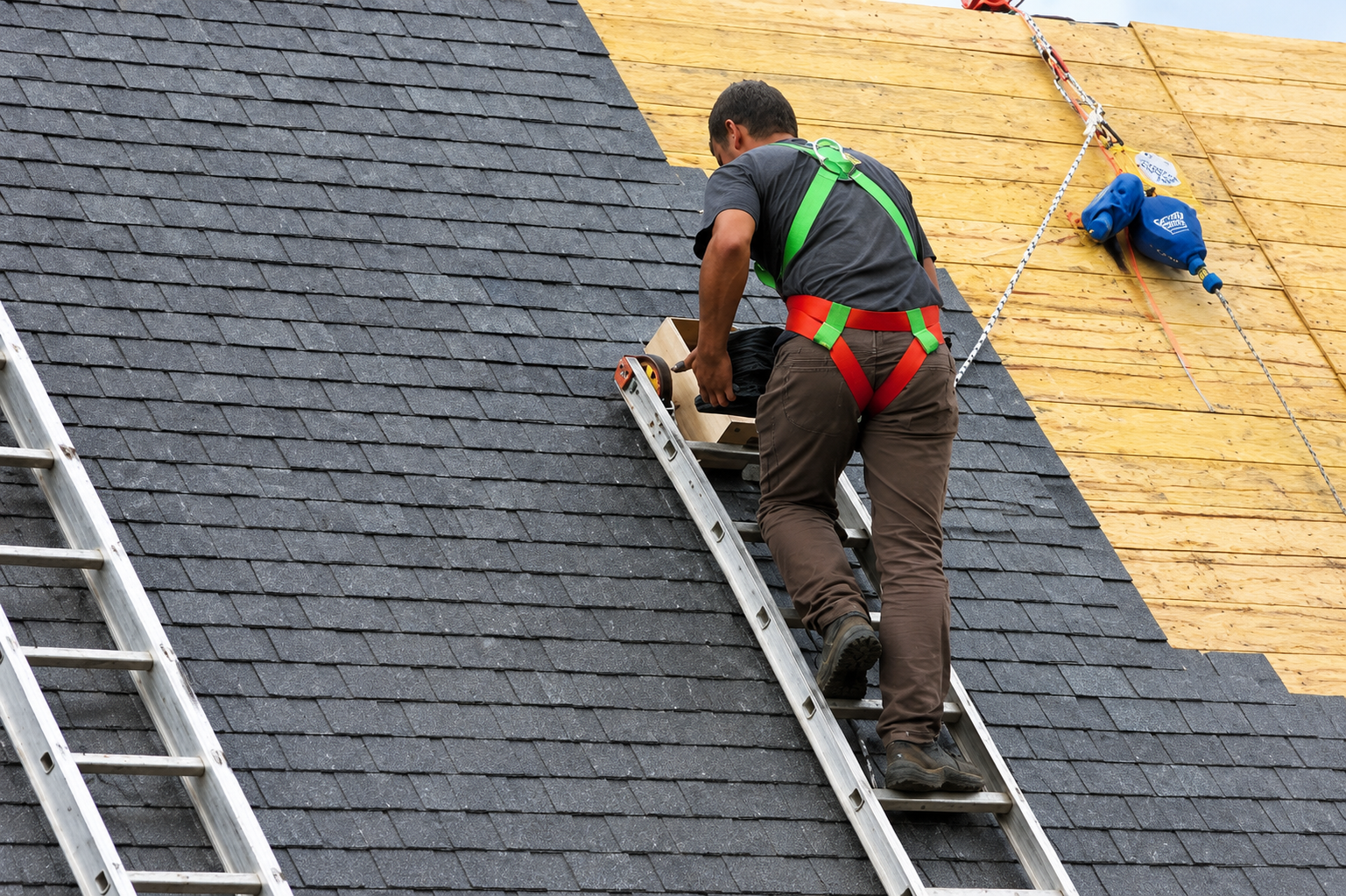 Roofer working on a shingle roof with a safety harness